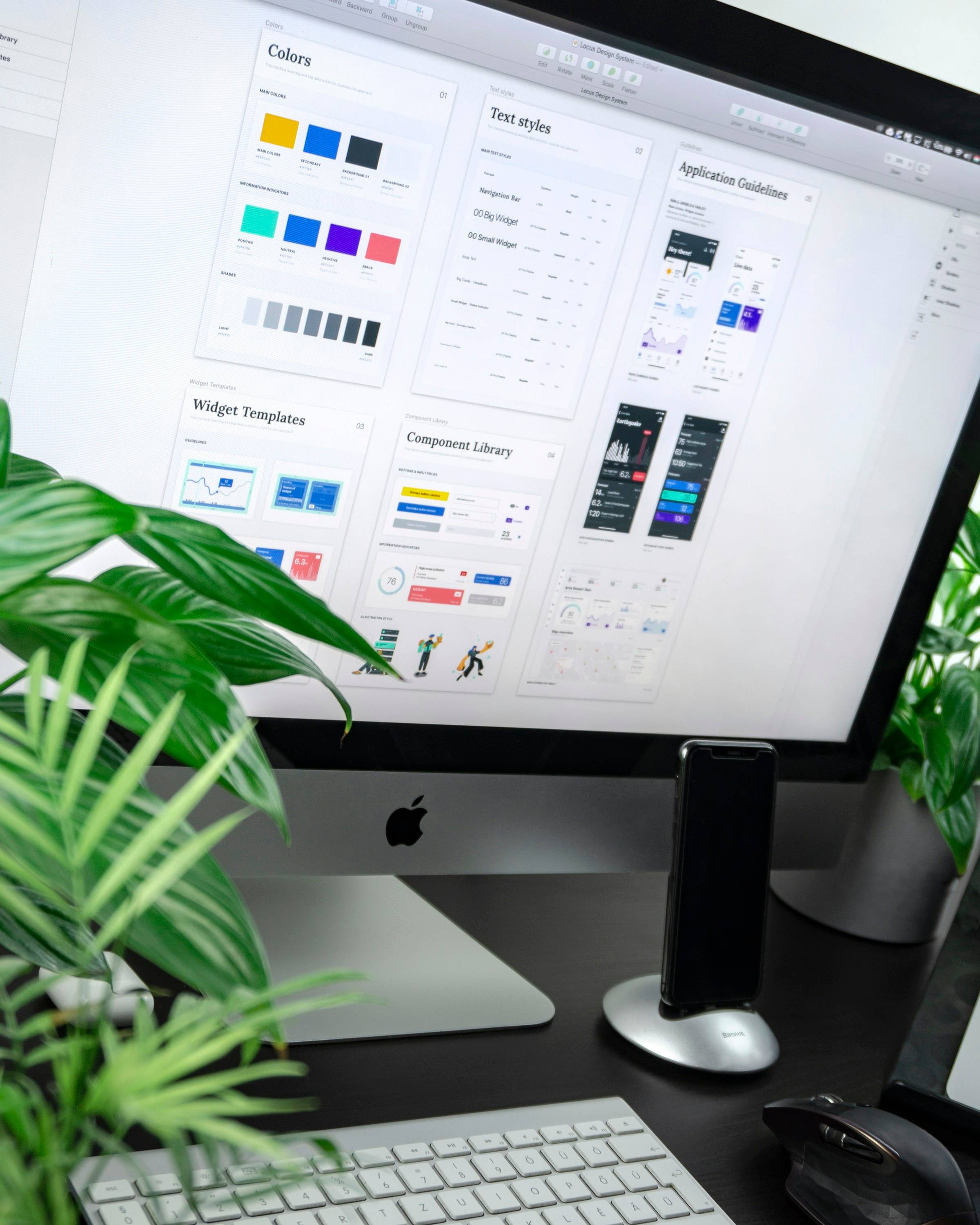 Monitor mit Bausteinen eines Website-Designsystems, davor Zimmerpflanzen auf dem Schreibtisch